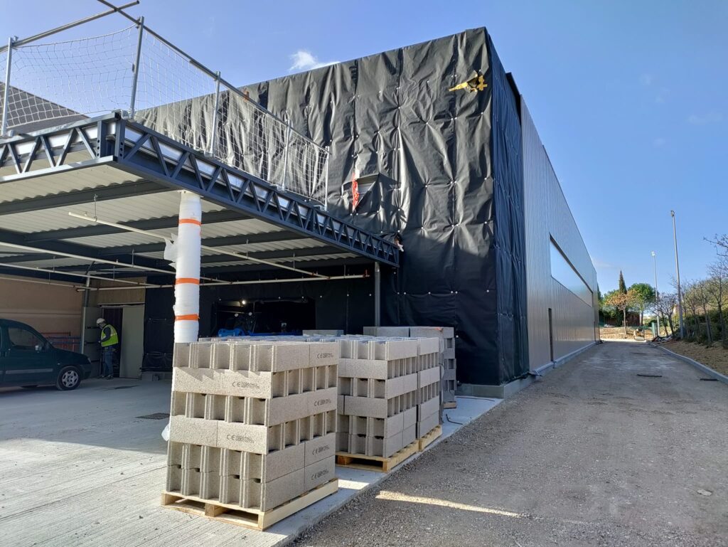 Chantier de construction avec parpaings CE et bâtiment industriel en travaux sous un ciel bleu dégagé.