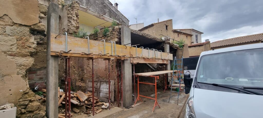 Rénovation structurelle avec étaiement de poutres et colonnes en béton sur un vieux bâtiment en pierre.