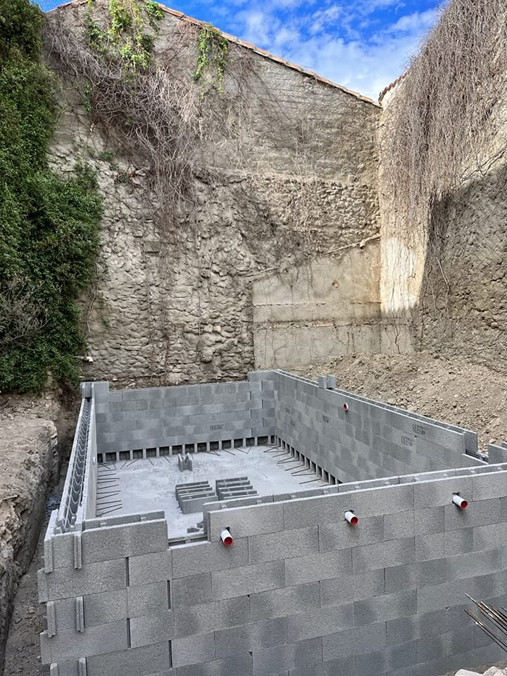 Fondation et murs en blocs BCI : l'étape cruciale de la construction. Structure de fondation en blocs de coffrage isolant (BCI) dans une excavation profonde. Murs de soutènement de pierre et ciel bleu.