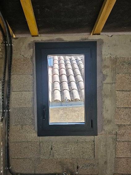 Fenêtre noire sur mur parpaing vue toit tuiles.